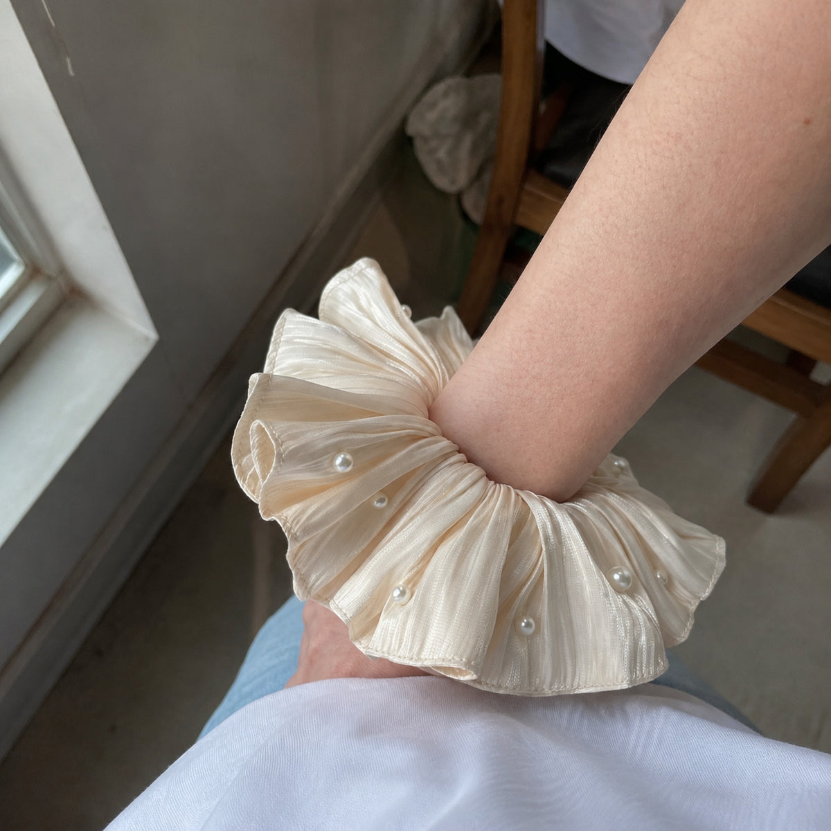 Oversized ivory hair accessory worn around the wrist to show its full gathered shape and elegant pearl accents.