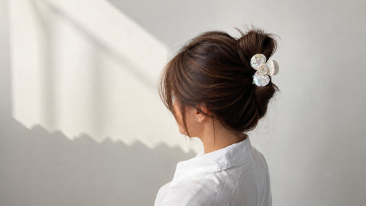 White camellia flower hair claw securing brunette hair in a relaxed updo with soft natural window light.