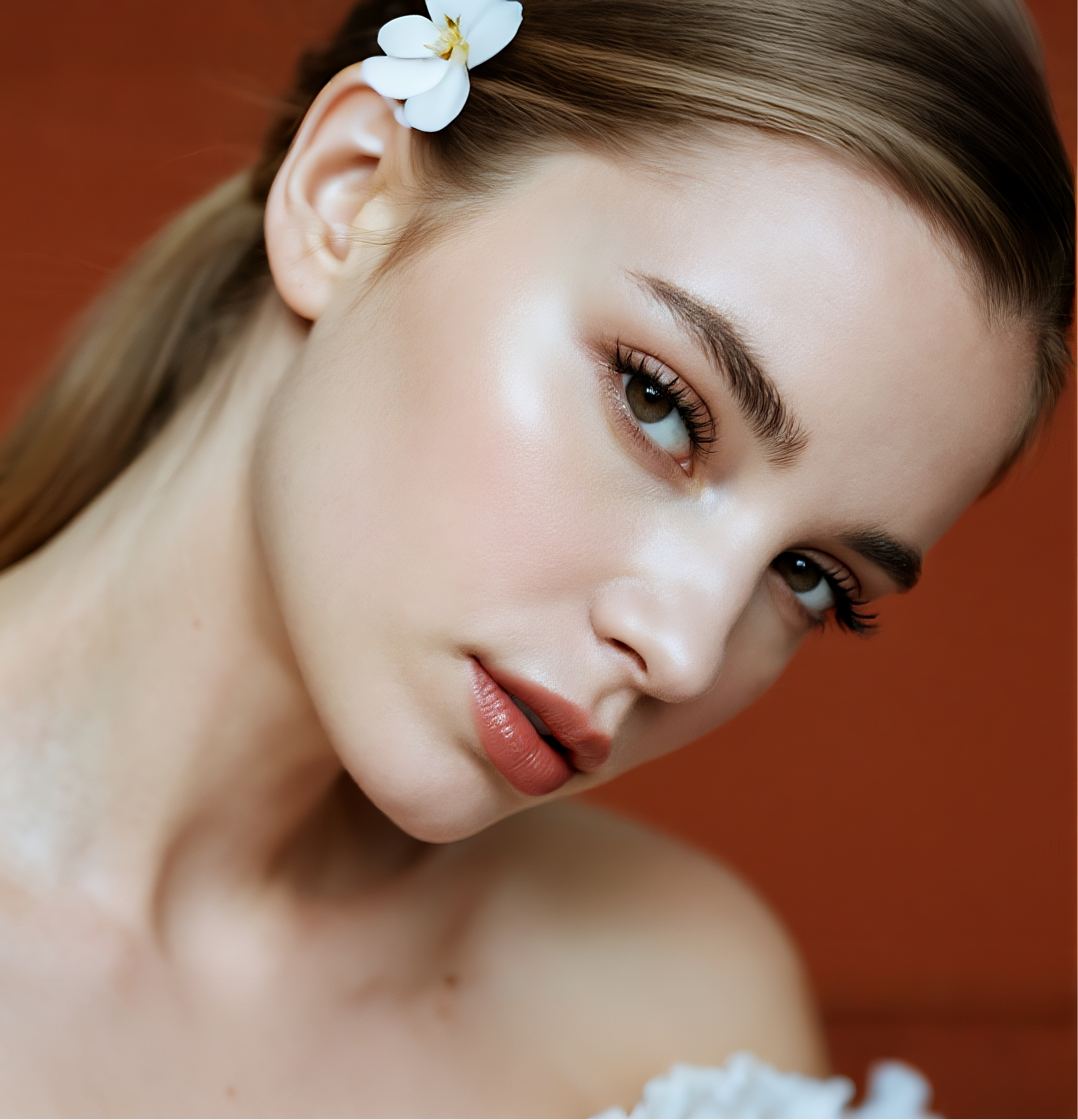 Portrait side close-up with false lashes applied; floral hair accessory and soft lighting create a natural, soft-glam finish (warm orange backdrop)
