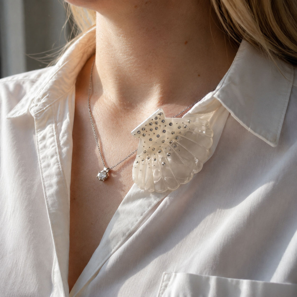 Sparkling white shell hair clip attached to a white shirt collar as an elegant coastal fashion accessory.