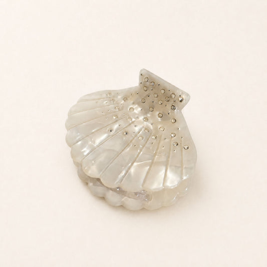 Angled view of a handmade scallop shell hair accessory featuring luminous swirls, raised ridges and crystal embellishments.