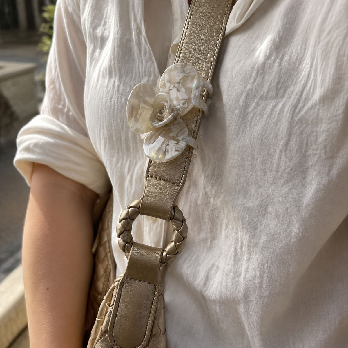 Handmade floral hair clip attached to a taupe shoulder bag strap as an elegant pearlescent decorative accessory.

